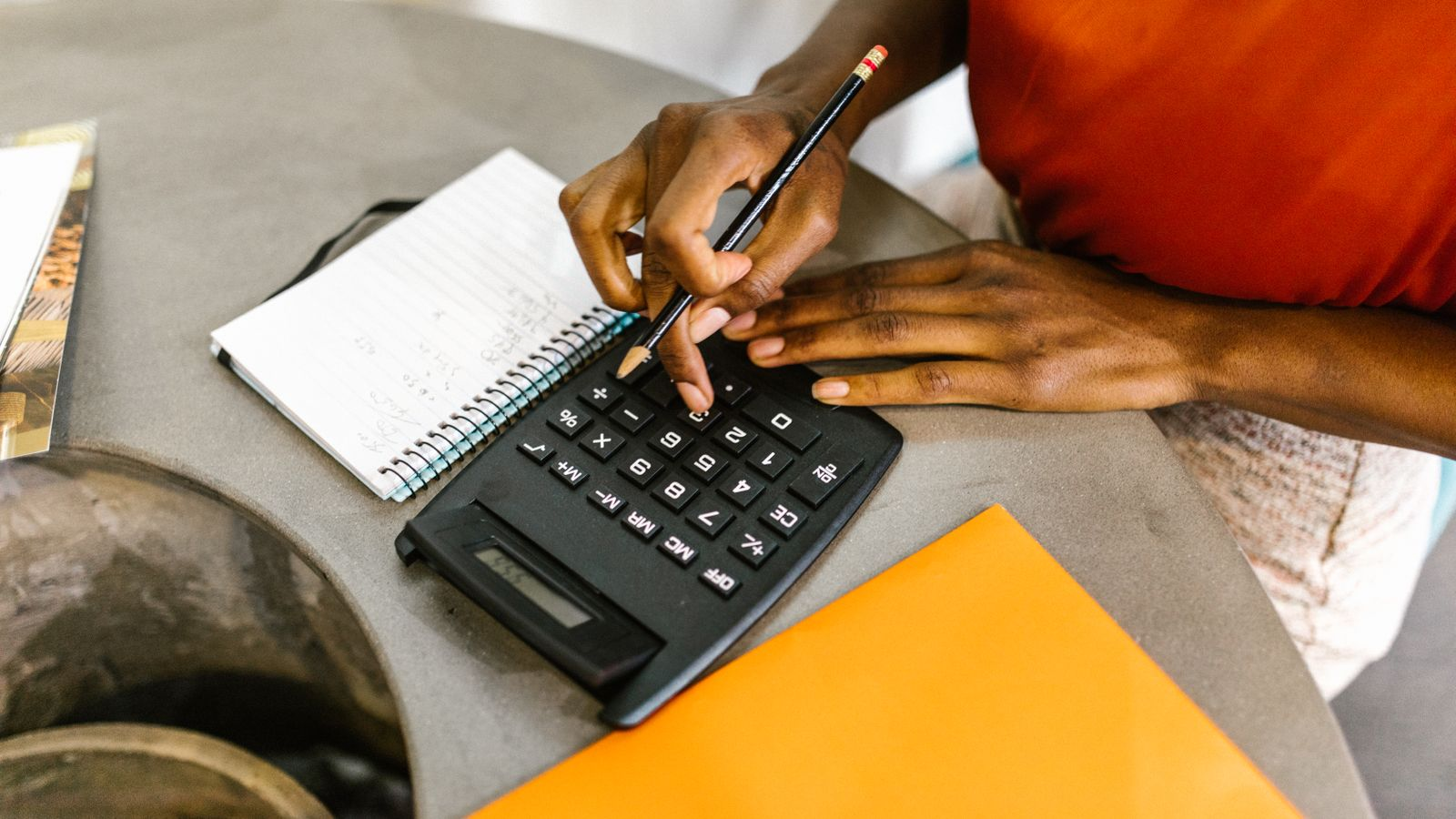 Using a calculator and notebook to check amounts, illustrating withdrawal cost calculations