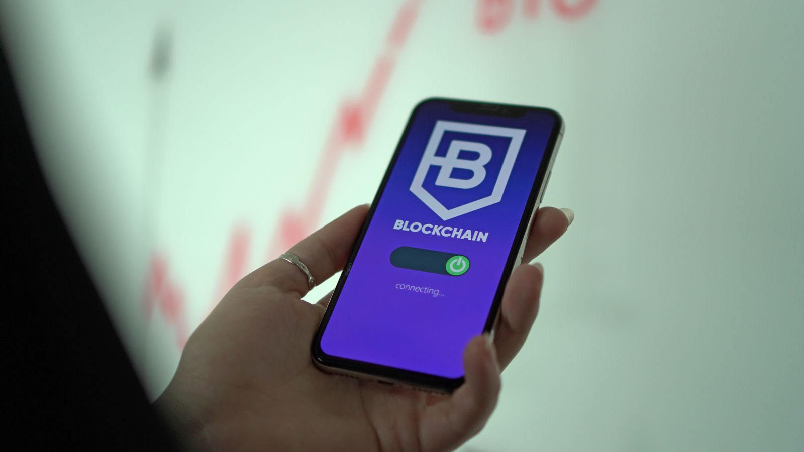 A hand holding a phone displaying a blockchain-themed app