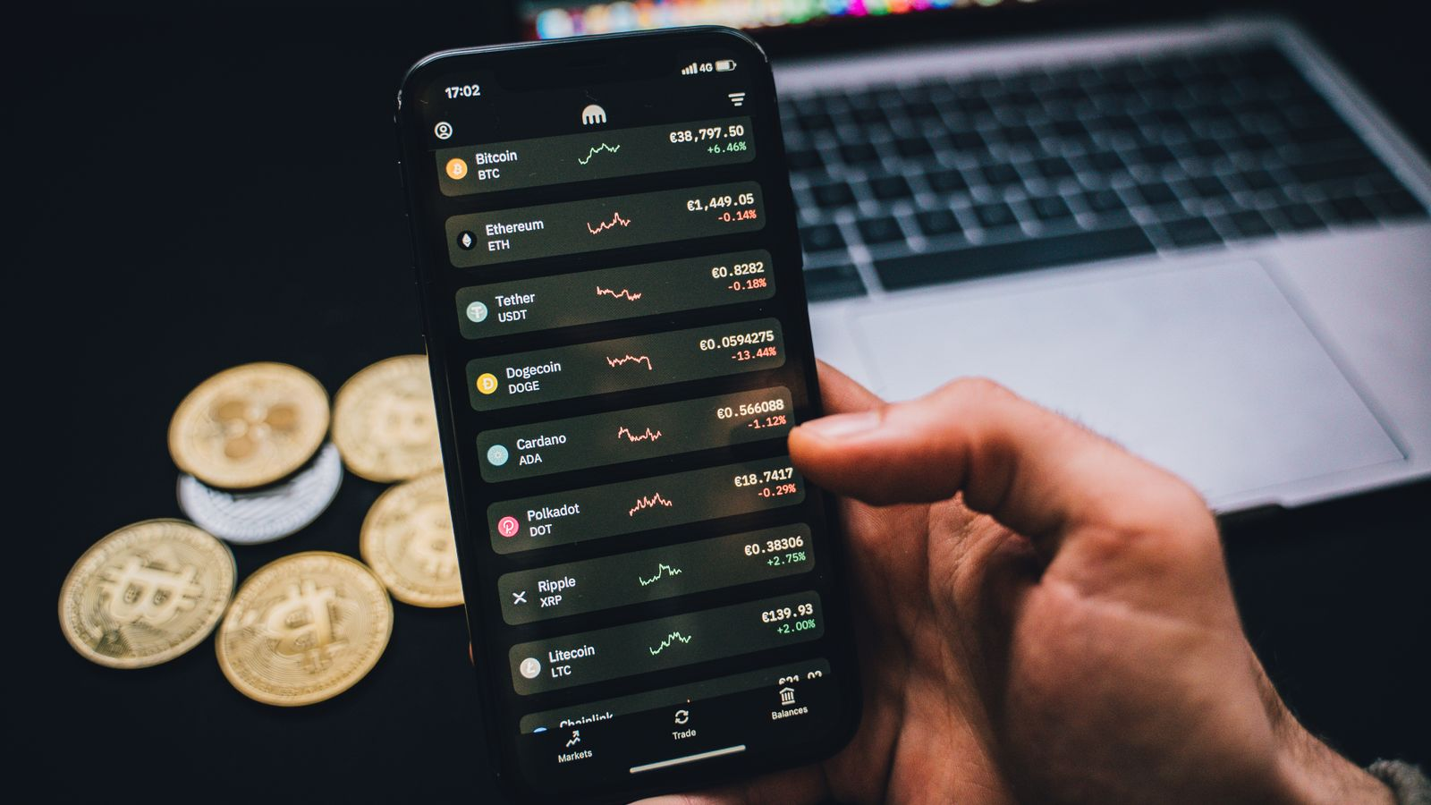 A person checking crypto information on a smartphone beside a computer