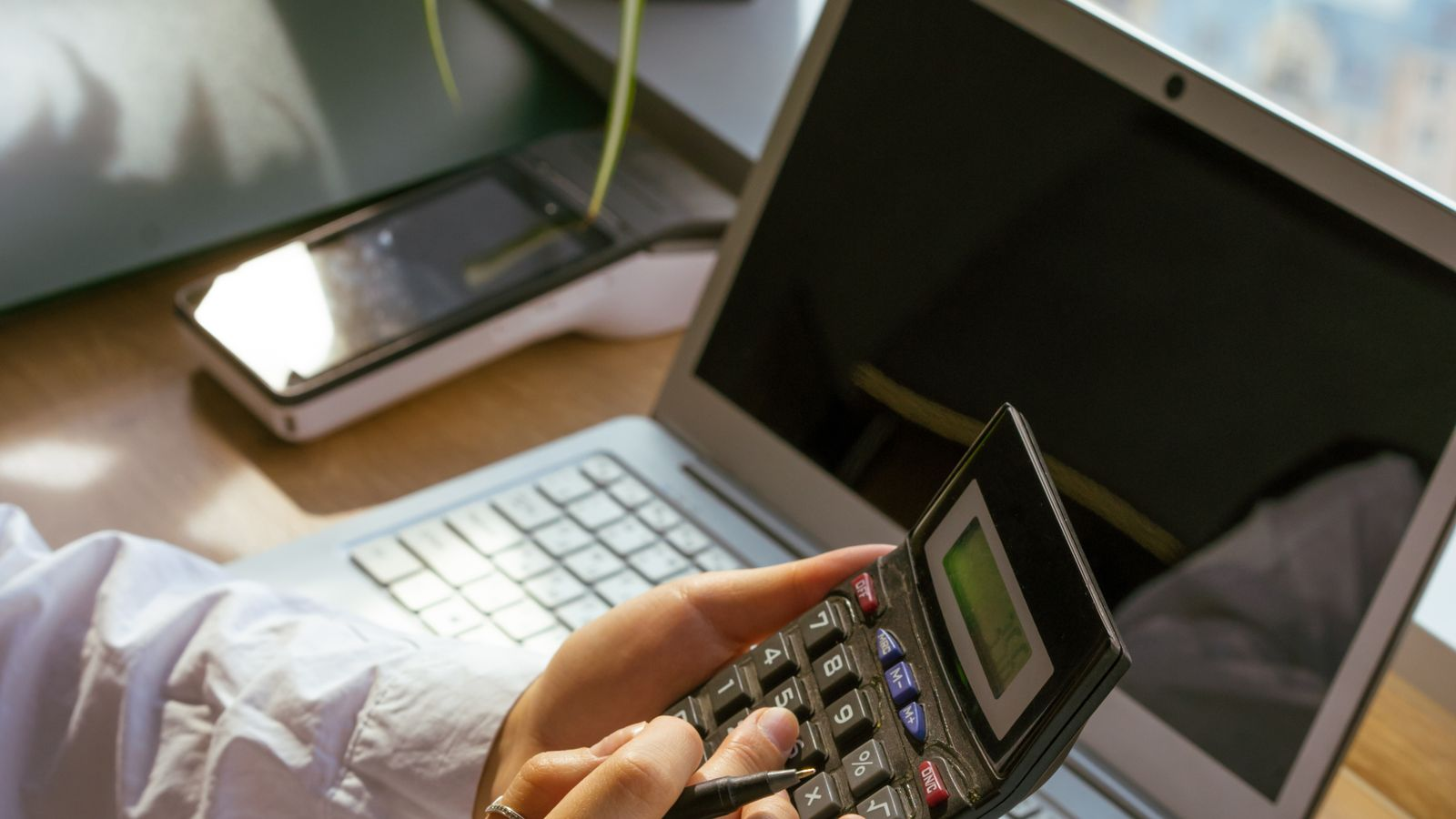 Using a calculator beside a computer to check payment amounts and an account budget