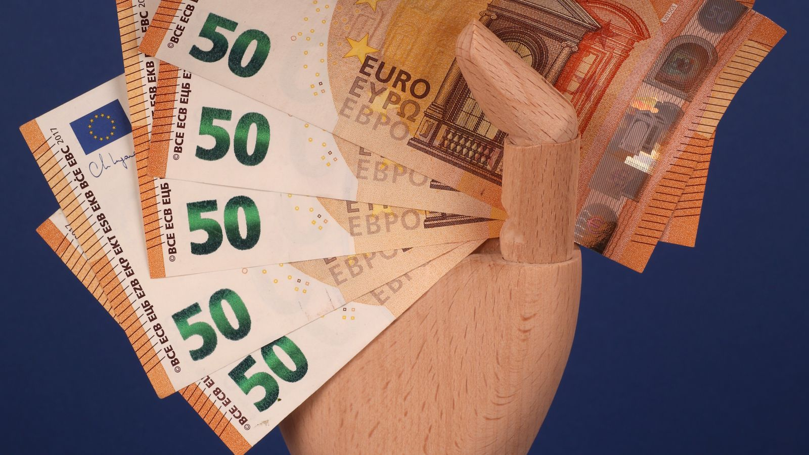 A wooden hand holding euro banknotes against a blue background