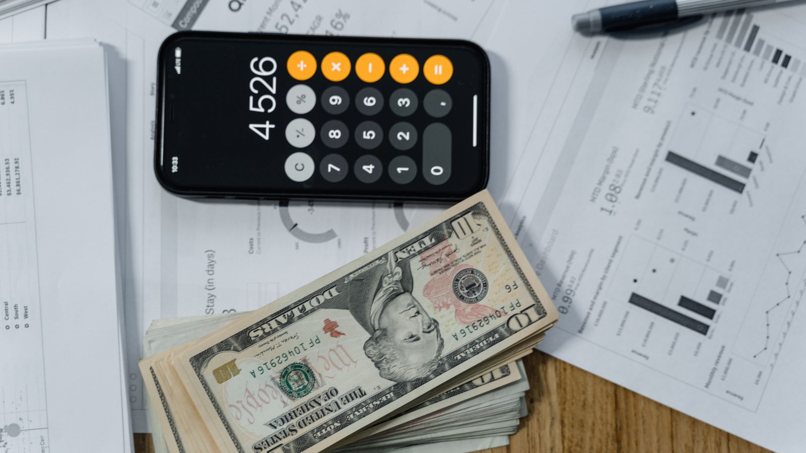 A phone calculator, dollar banknotes, and financial documents illustrating cost calculations